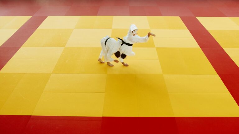 Two martial artists practicing judo techniques on a vibrant yellow and red mat.